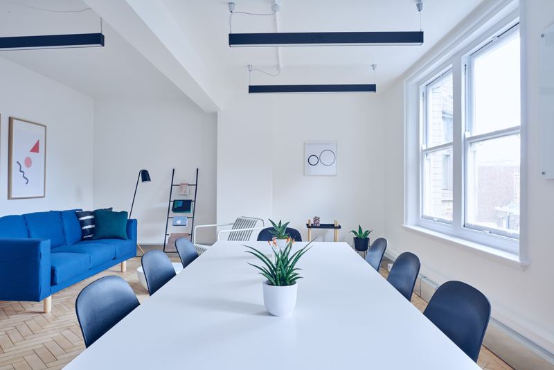 Symbolbild: helles Büro mit langem Besprechungstisch und blauem Sofa